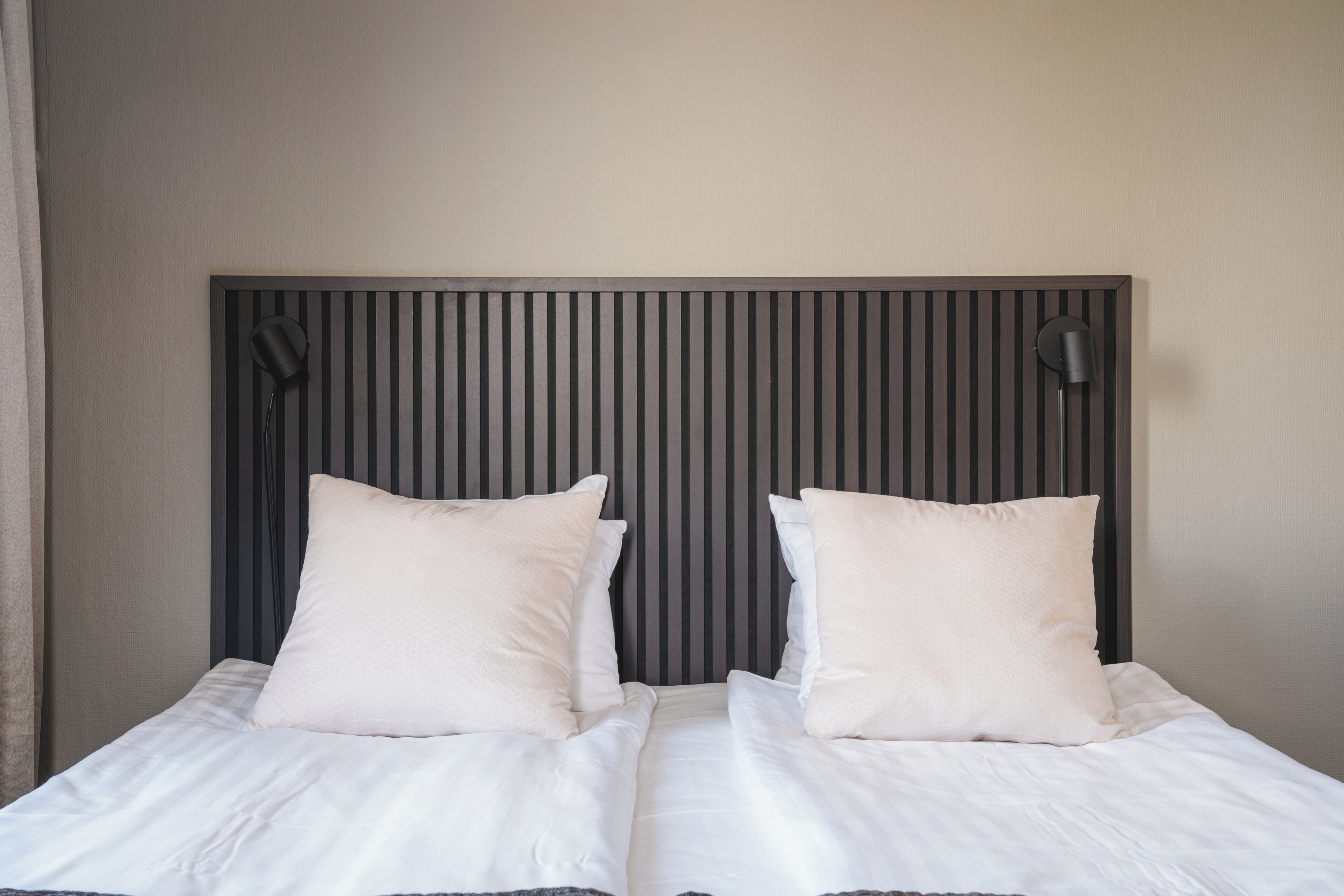 Cama doble con dos almohadas y cabecera con líneas verticales.