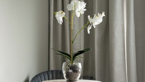 A hotel room with a bed, a chair, a small round table with a vase of white flowers, and a window with curtains. - VICI Hotels Linköping (Linkoping)
