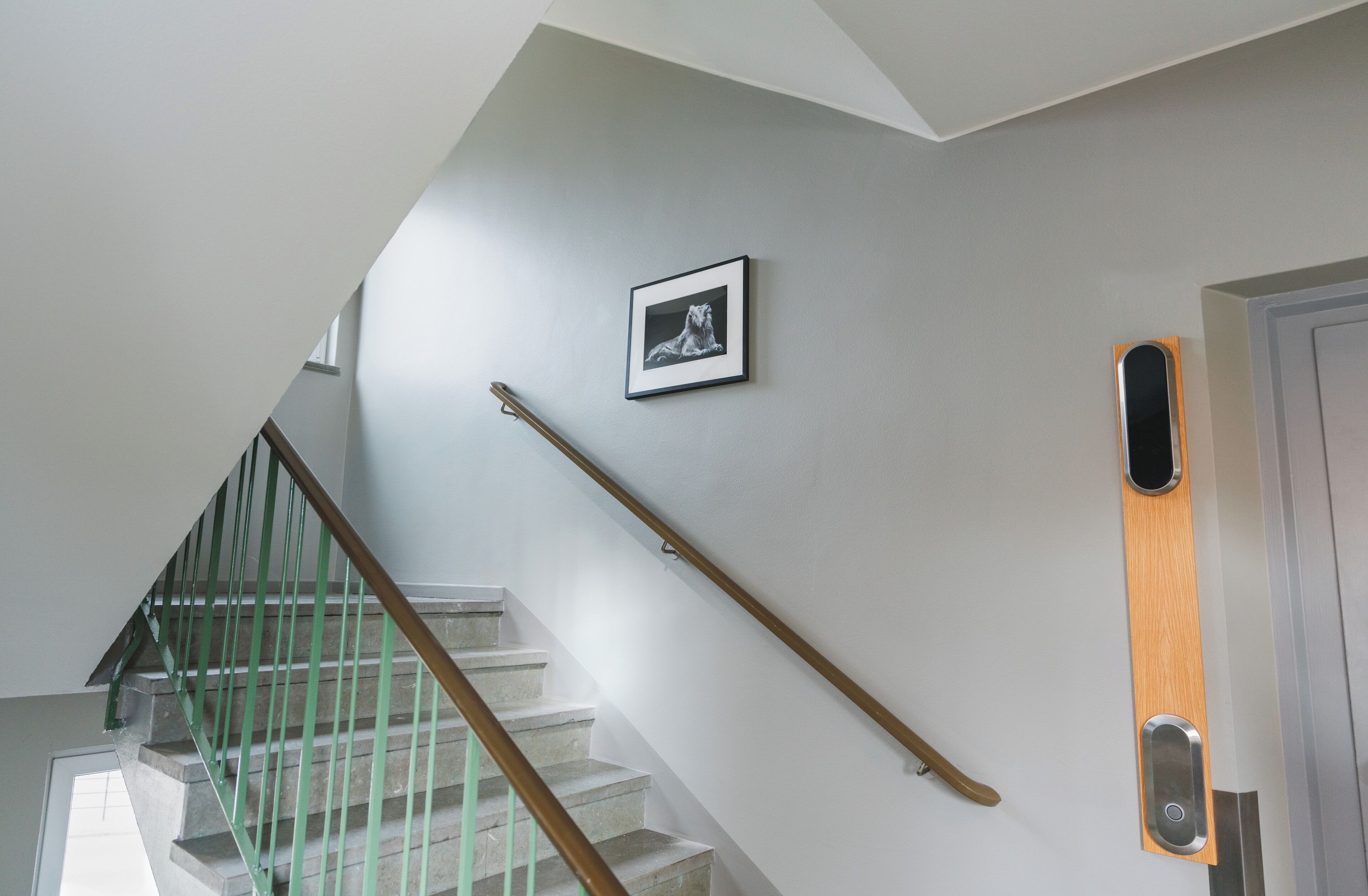 A staircase with a green handrail, a picture on the wall, and a door with a wooden panel.