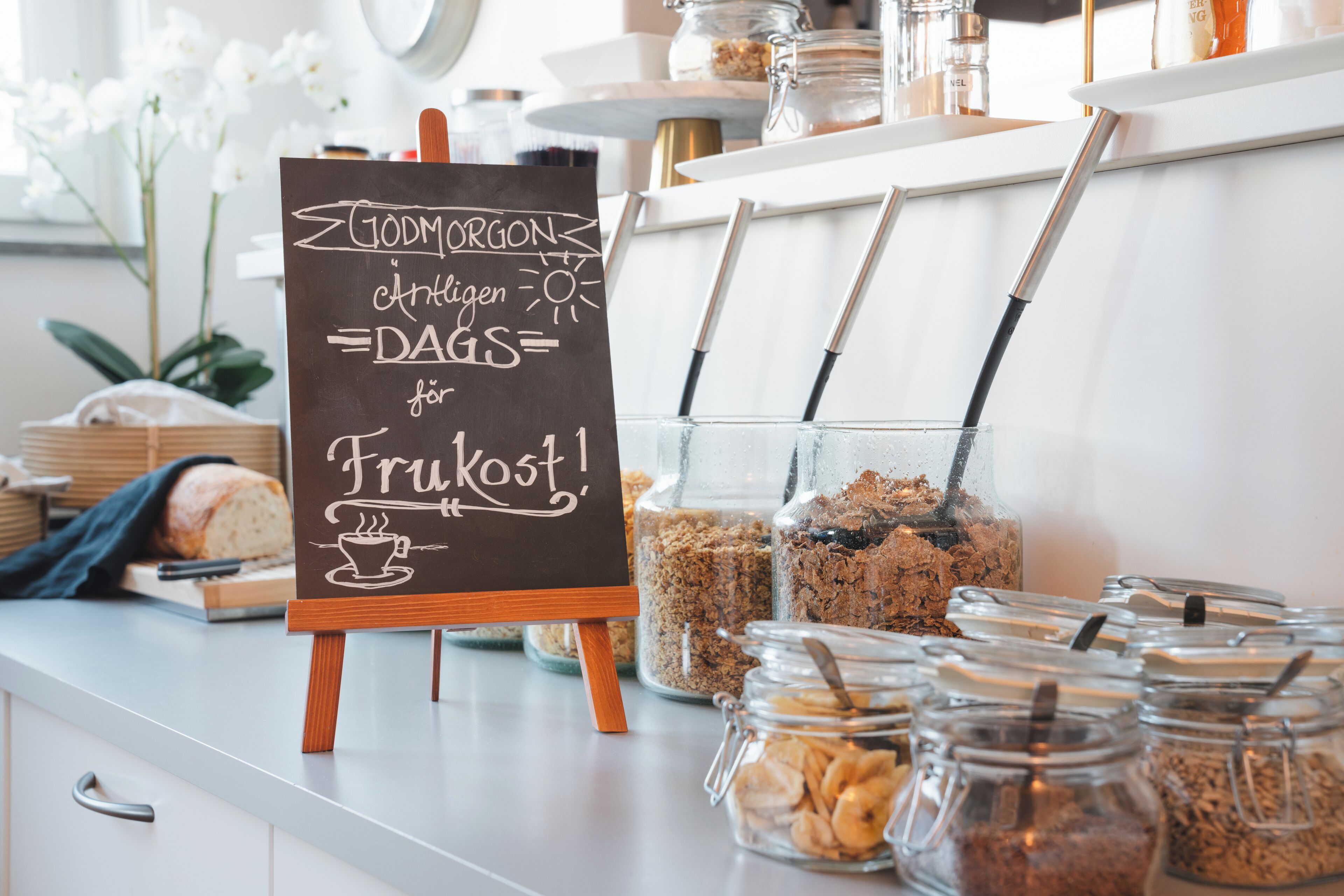 A breakfast buffet with a chalkboard sign, jars of granola, and a loaf of bread.