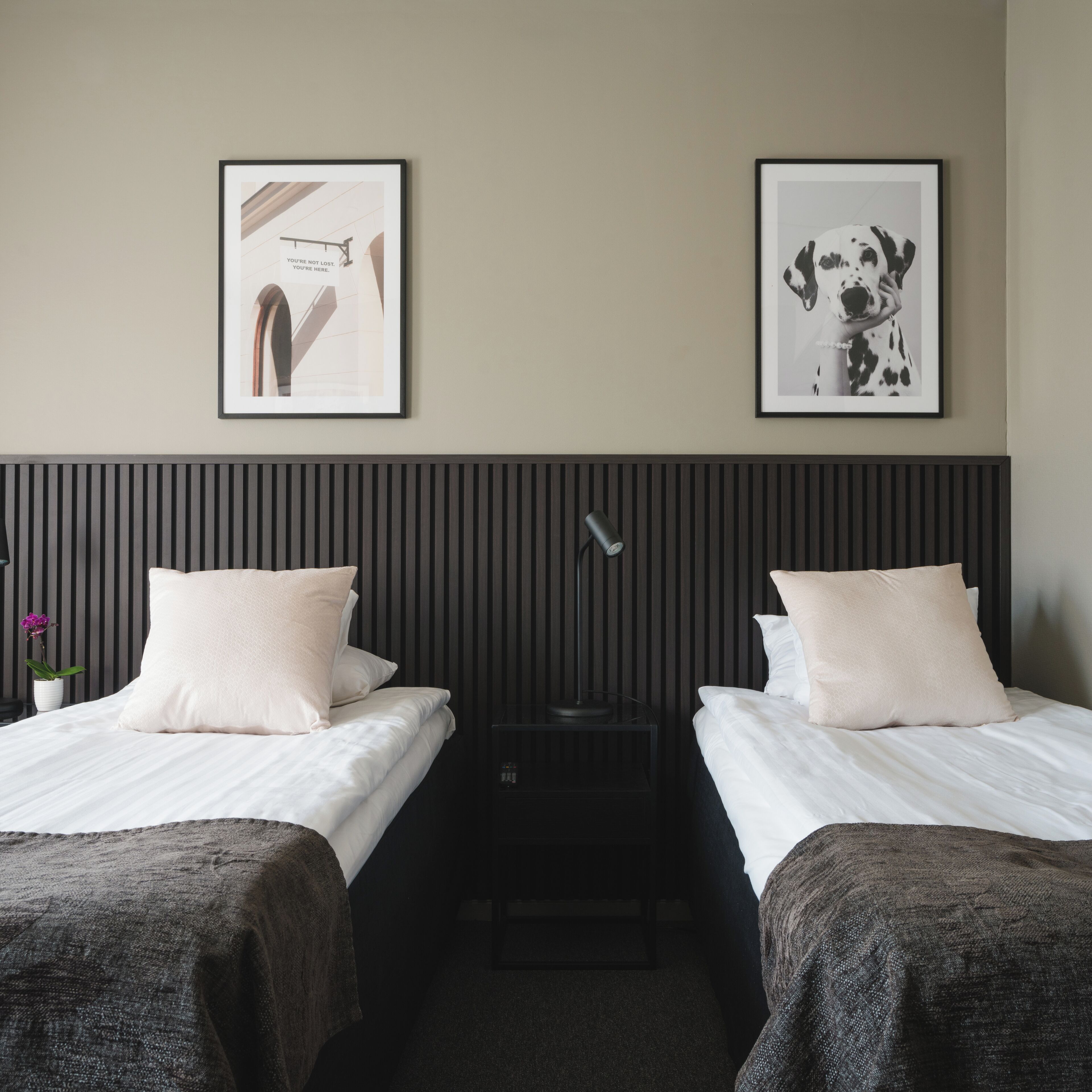 Camera d'albergo con due letti, un comodino, una lampada e due quadri appesi al muro.