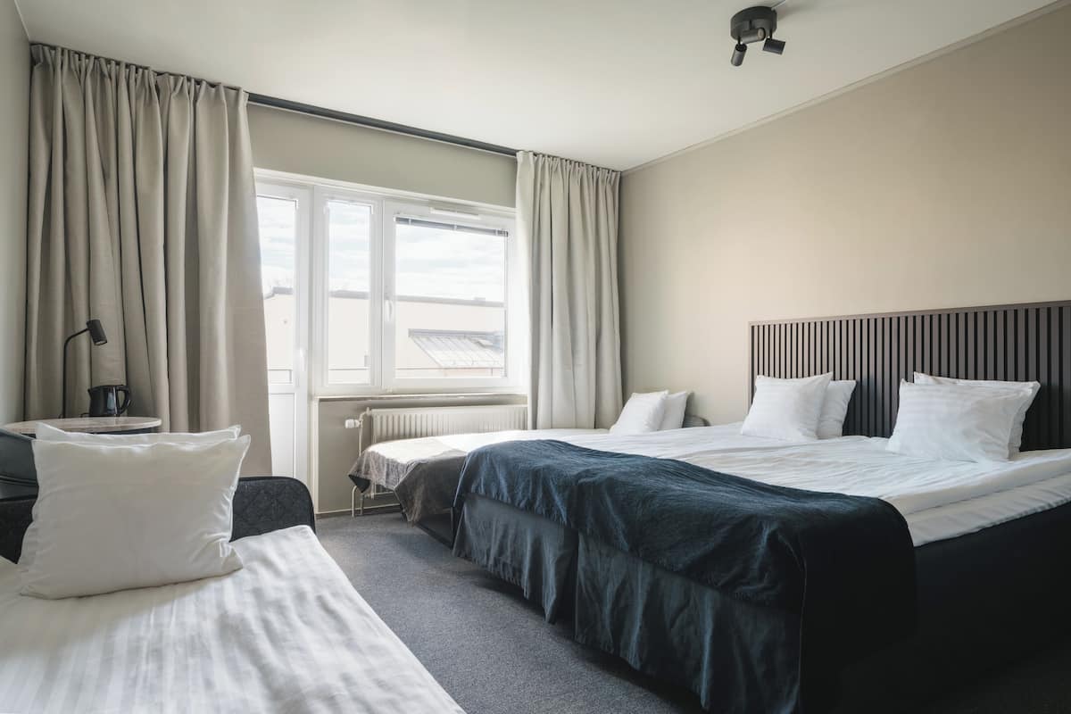 A hotel room with a large bed, a smaller bed, a desk with a chair, and a window with curtains.