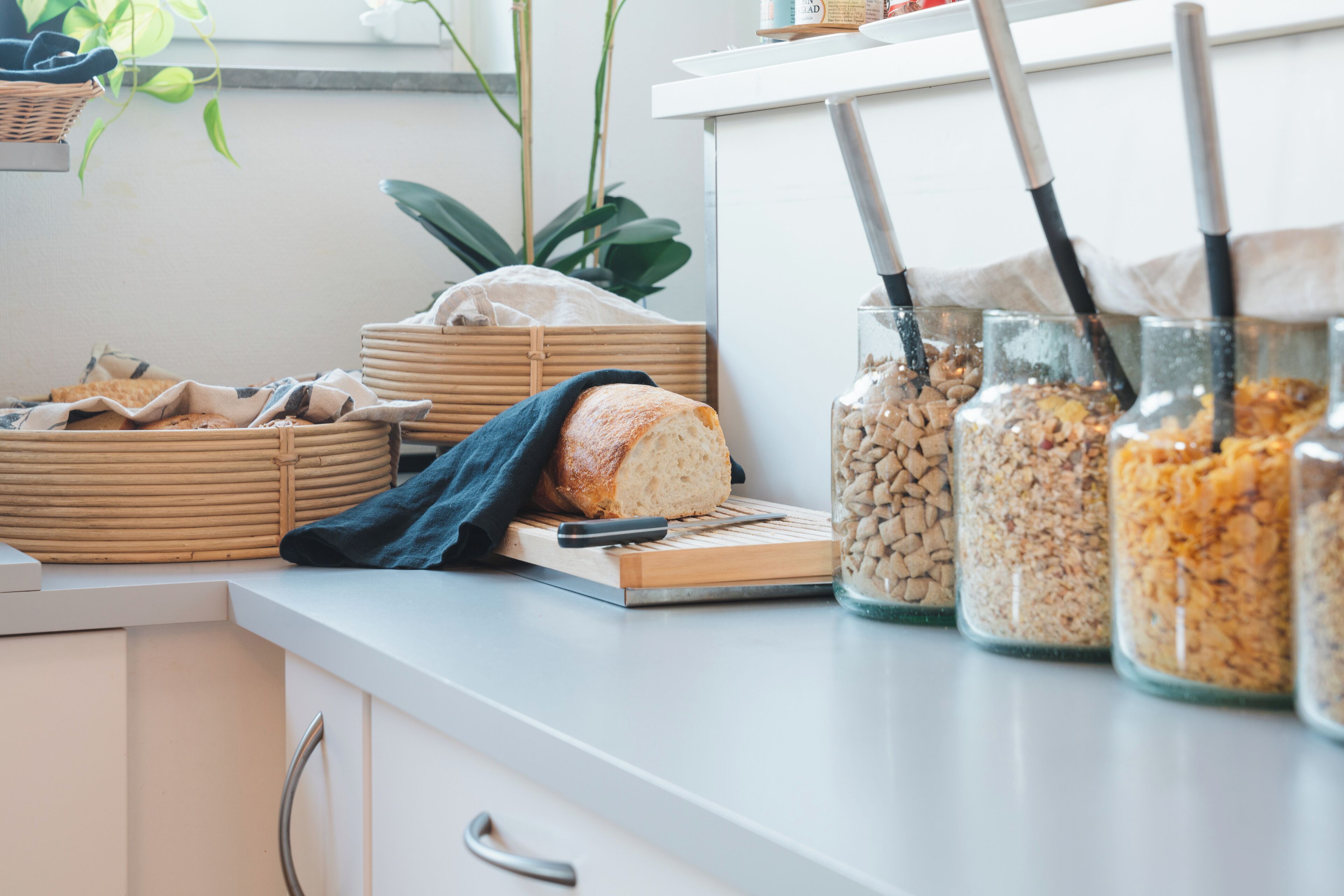 A kitchen counter with jars of grains, a loaf of bread, and a cutting board.