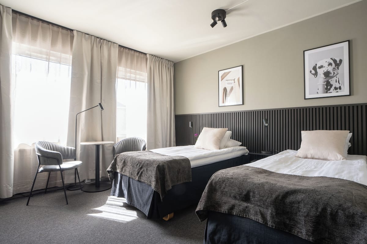 A hotel room with two beds, a desk, a chair, and a large window with curtains.