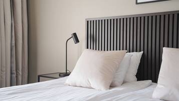Una cama bien hecha con sábanas y almohadas blancas, una lámpara de noche negra y un cabecero moderno con líneas verticales.