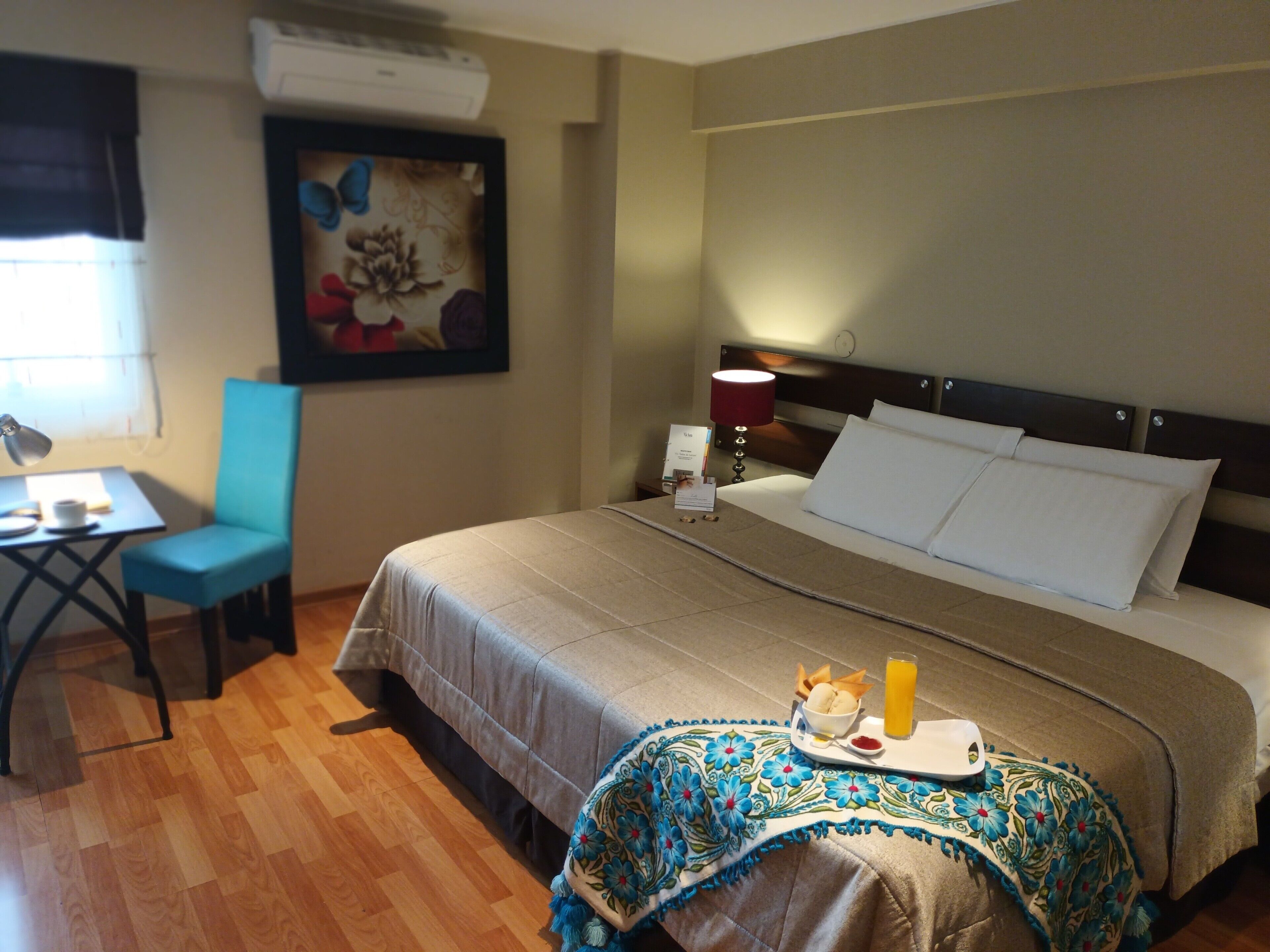 A hotel room with a bed, a desk with a chair, a lamp, and a painting on the wall.