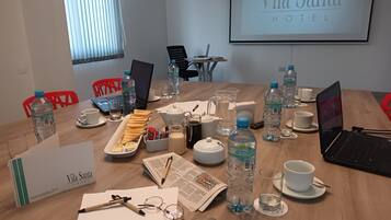 Uma sala de conferências no Vila Santa Hotel, com uma mesa de madeira preparada para uma reunião, laptops, garrafas de água e uma tela de projetor exibindo o nome do hotel.