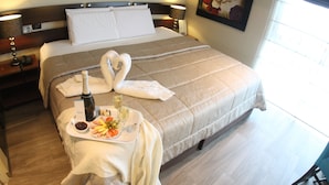 Una cama bien hecha con una colcha marrón, una bandeja con champán, copas y una bandeja de frutas.