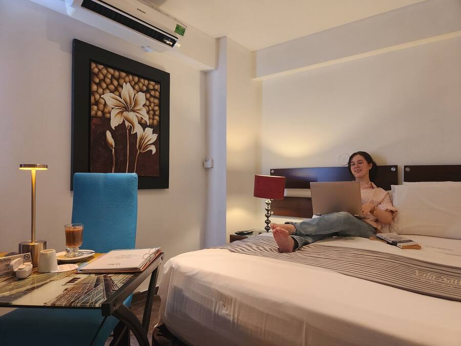 Una habitación de hotel con una cama, un escritorio con una computadora portátil, una obra de arte floral enmarco y una lámpara de pie.