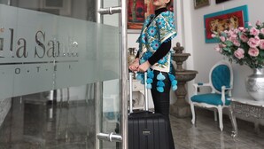Un vestíbulo de hotel con puerta de cristal, una maleta negra y una persona de pie junto a la puerta.