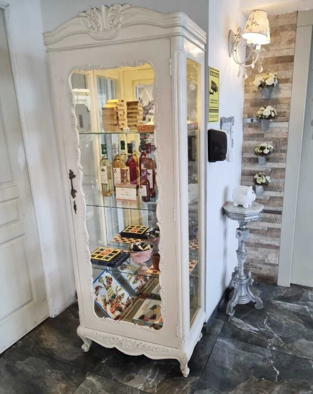 Un meuble blanc, richement décoré, doté de portes en verre derrière lesquelles on peut apercevoir divers objets.
