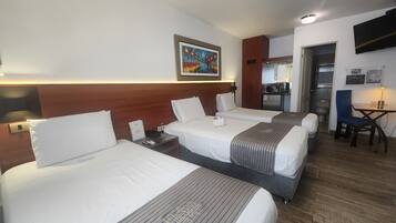 A hotel room with three beds, a desk, a chair, a TV, and a painting on the wall.