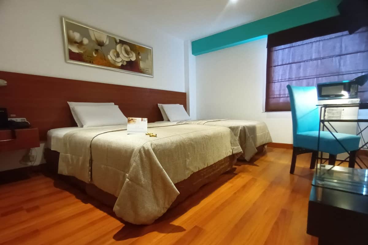 A hotel room with two beds, a desk with a chair, a painting on the wall, and a window with curtains.