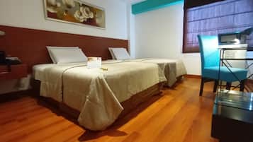 Habitación de hotel con dos camas, un escritorio con silla, un cuadro en la pared y una ventana con cortinas.