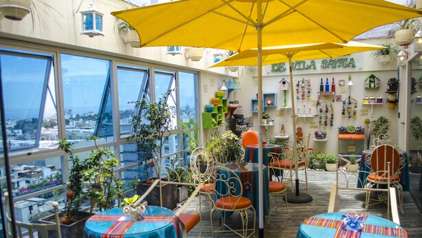 Una terraza en la azotea con mesas y sillas, plantas en macetas y vistas de la ciudad.