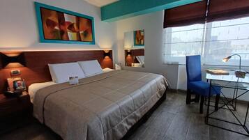 Una habitación de hotel con cama, mesita de noche, lámpara, silla, escritorio y ventana.