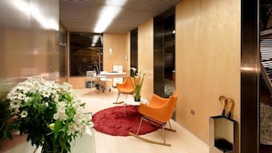 A modern interior with a dining area, a red rug, and orange chairs. - Hotel Holos (Seville)