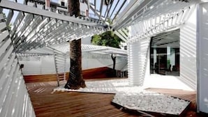 A modern interior with a wooden floor, white structural elements, and a glass door leading to an outdoor area. - Hotel Holos (Seville)