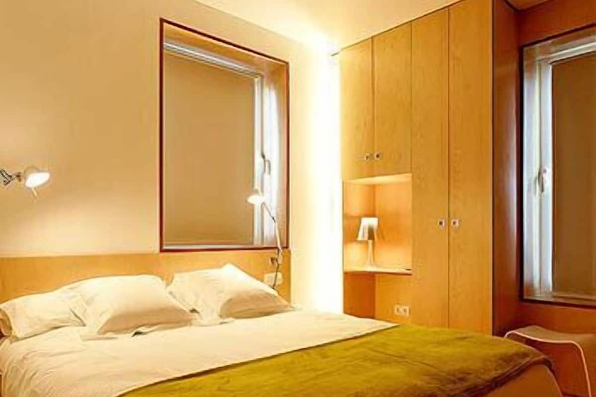 A bedroom with a bed, a nightstand, a wardrobe, and a window.