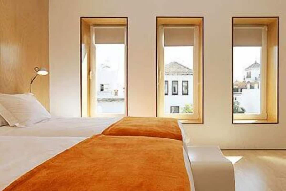 A room with a bed, a bench, and three windows.