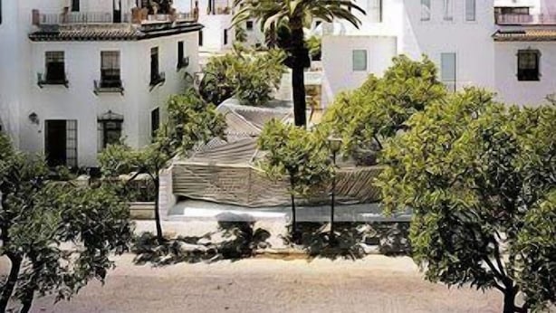 A courtyard with white buildings, a palm tree, and a covered area. - Hotel Holos (Seville)