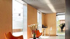 A modern interior with orange chairs, a red rug, and a vase of flowers. - Hotel Holos (Seville)