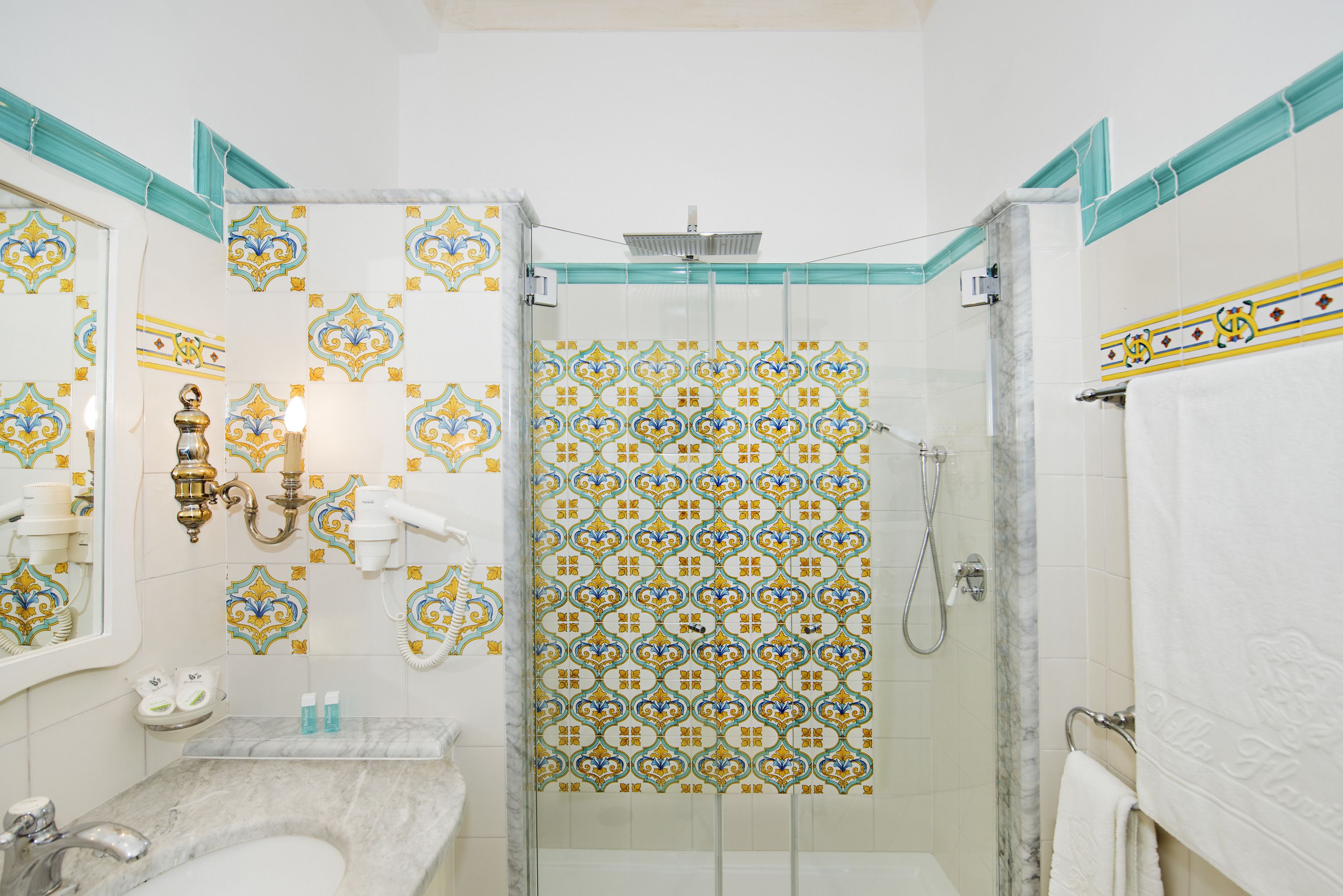 A bathroom with a marble sink, a glass shower enclosure, and decorative tiles.