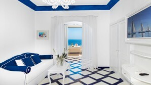 A room with a white sofa, a small table, a chandelier, a view of the sea, and a painting of sailboats. - Villa Flavio Gioia (Positano)