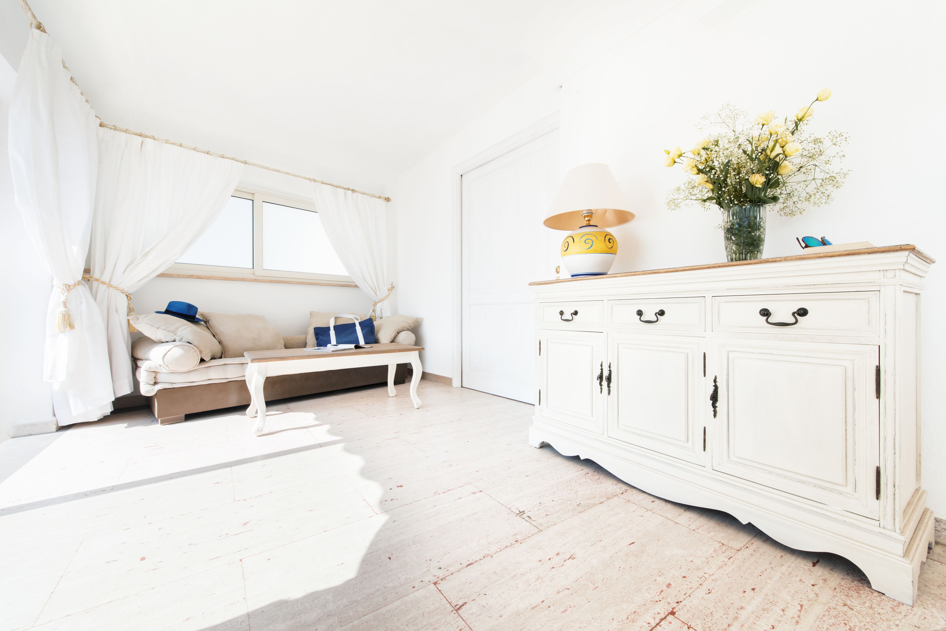 Une pièce lumineuse avec un canapé blanc, une petite table et un meuble blanc orné d’un vase de fleurs.