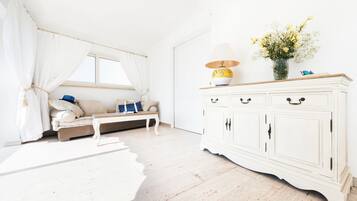 Une pièce lumineuse avec un canapé blanc, une petite table et un meuble blanc orné d’un vase de fleurs.