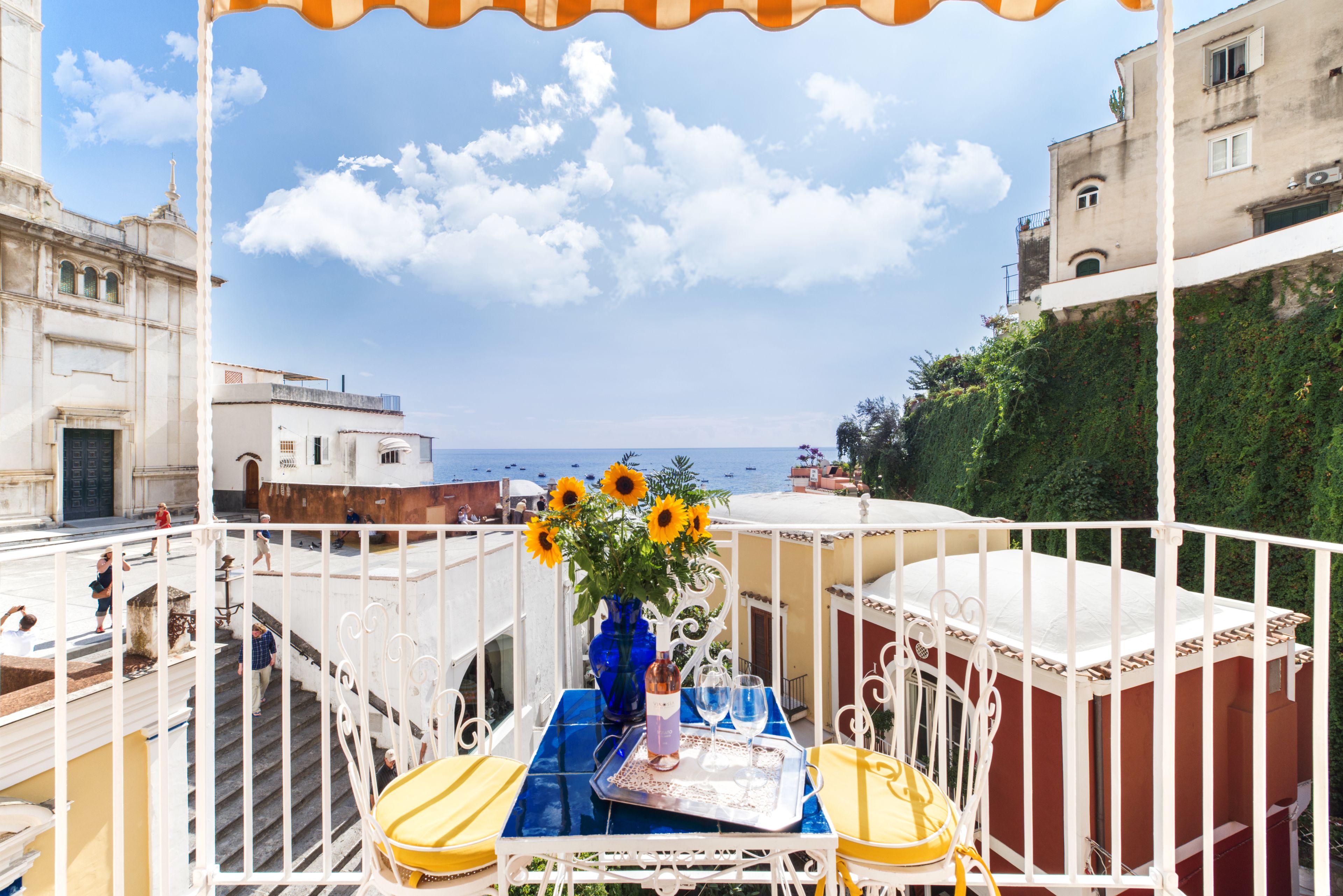 Un balcone con un tavolo apparecchiato per due persone, un vaso con girasoli e vista sul mare.