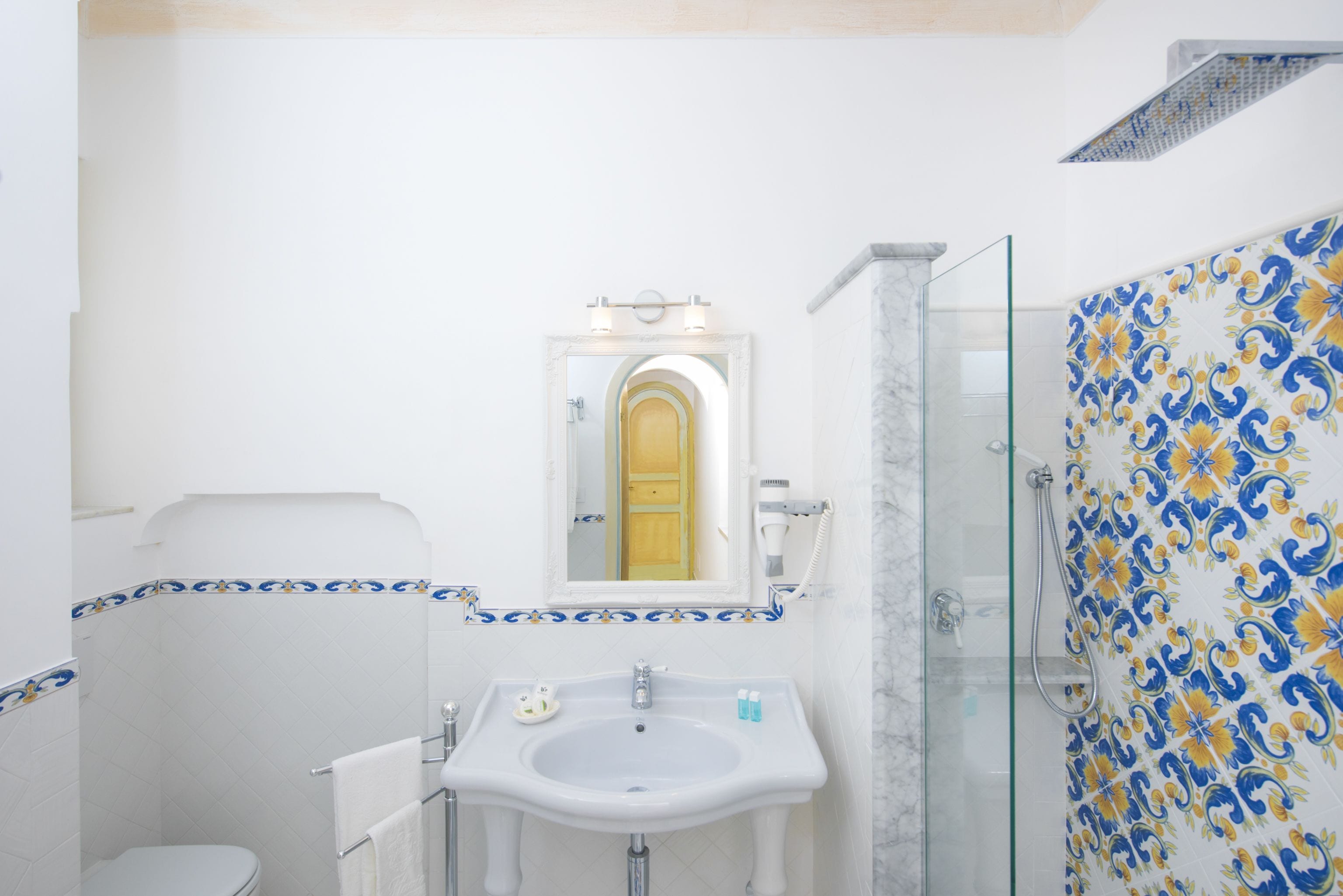 A bathroom with a white sink, a mirror, and a shower with blue and yellow tiles.