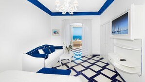 A hotel room with a white and blue color scheme, a sofa, a TV, and a view of the sea. - Villa Flavio Gioia (Positano)