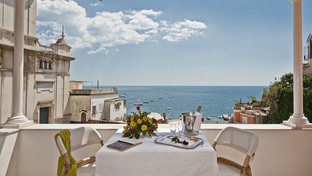 A table set with a vase of flowers, a bottle of champagne, and a tray with glasses, overlooking a coastal view with boats and historic buildings. - Villa Flavio Gioia (Positano)