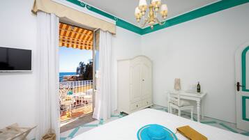 A bedroom with a bed, a wardrobe, a desk, and a view of the sea through a sliding door.
