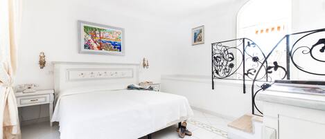A white bedroom with a bed, a nightstand, a dresser, and a mirror.