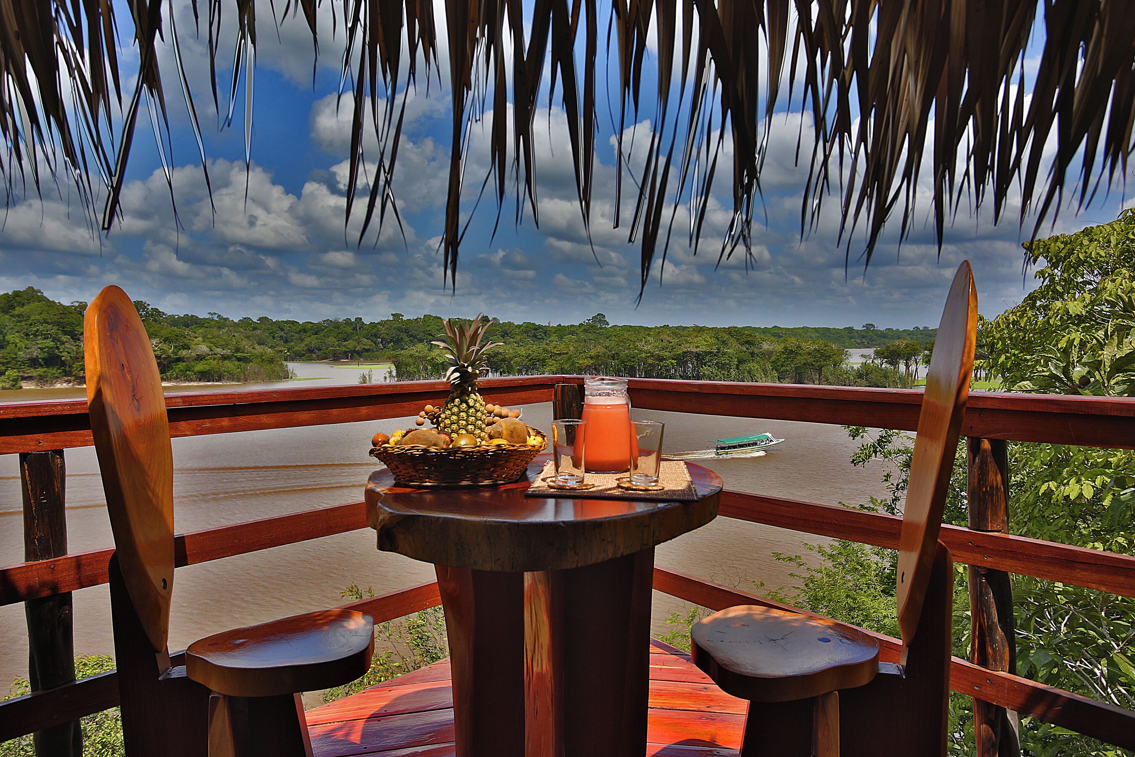 A wooden deck with a table set for two, overlooking a river and greenery.