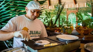 A person in a white uniform with a logo, preparing food on a portable stove in a tropical setting with lush greenery. - Juma Amazon Lodge (Autazes)
