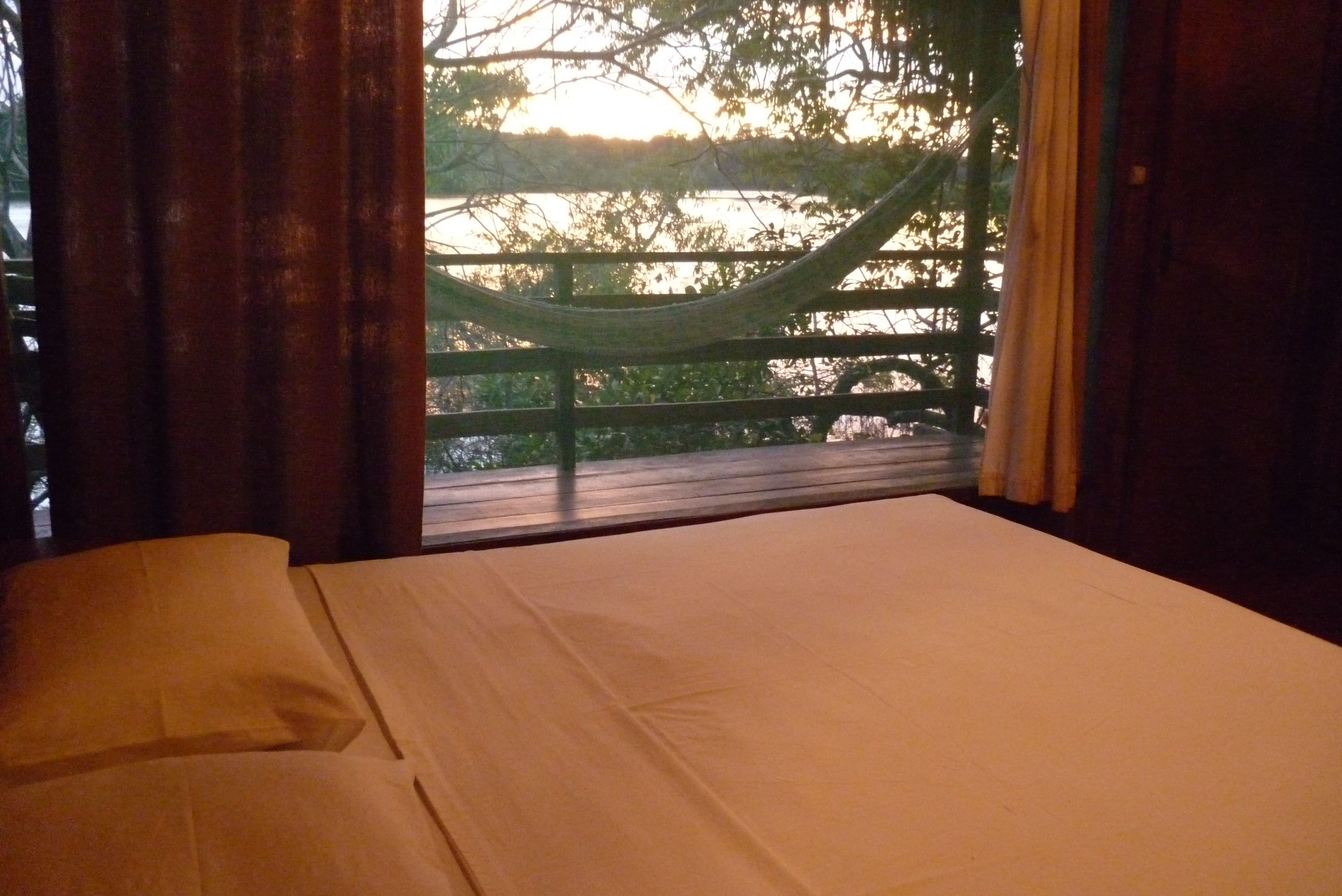 A bed with a view of a wooden deck and trees.