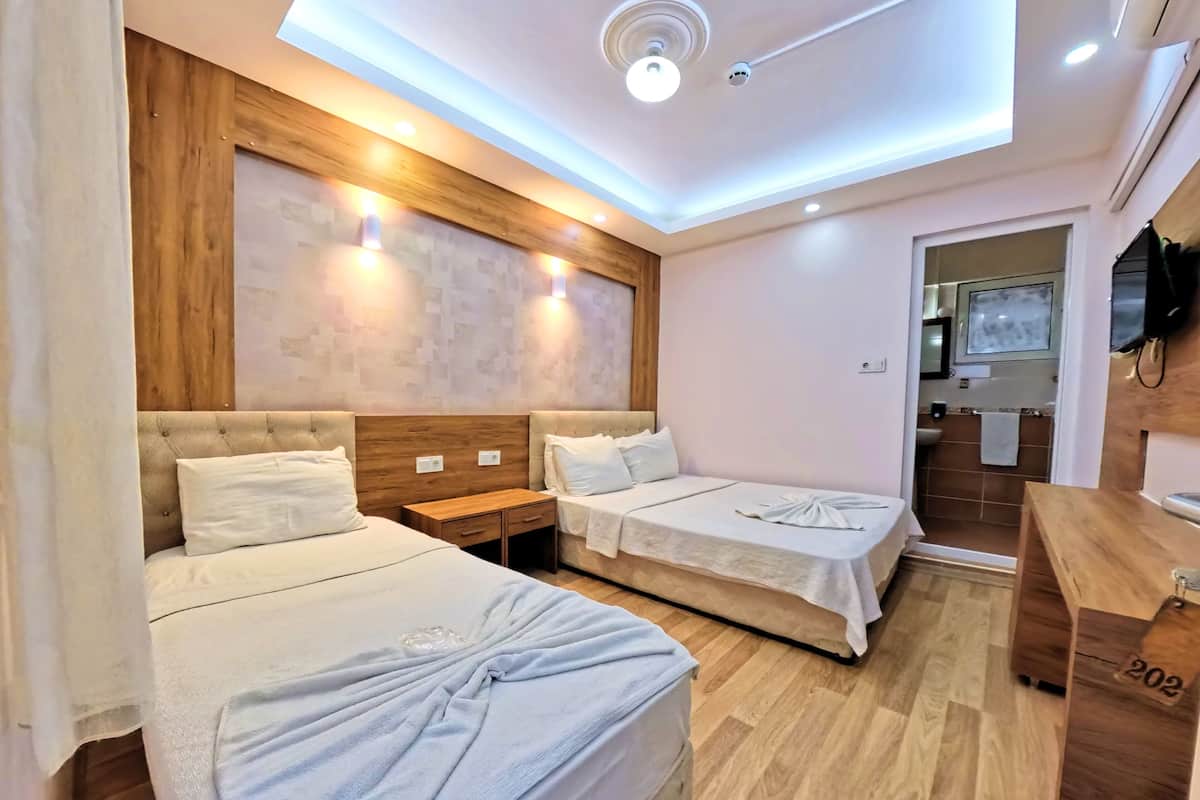 A hotel room with two beds, a wooden headboard, a ceiling light, and a wooden desk.