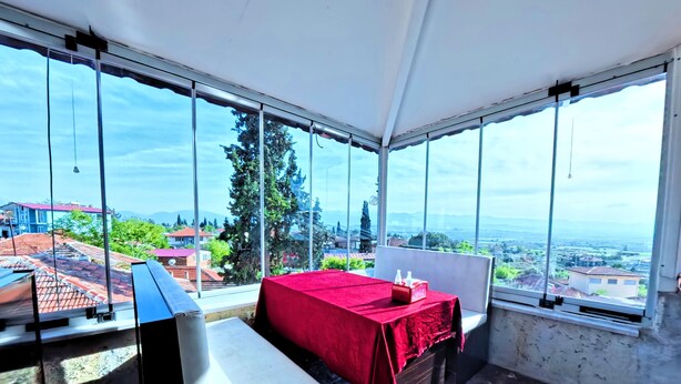 A room with a bed, a bench, and large windows offering a city view. - Goreme Sakura  (Denizli)