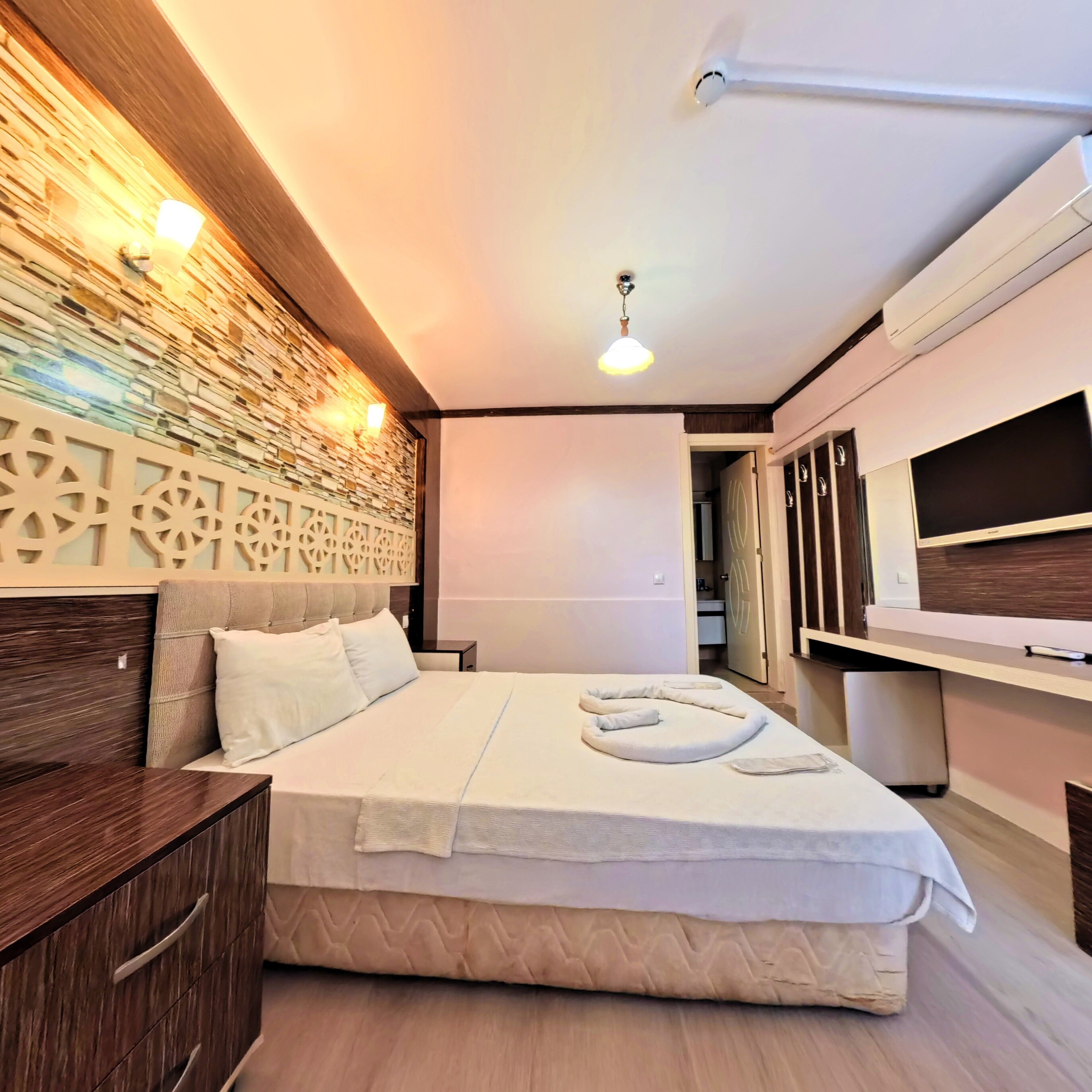 A modern bedroom with a bed, bedside tables, a wall-mounted light, and a TV.