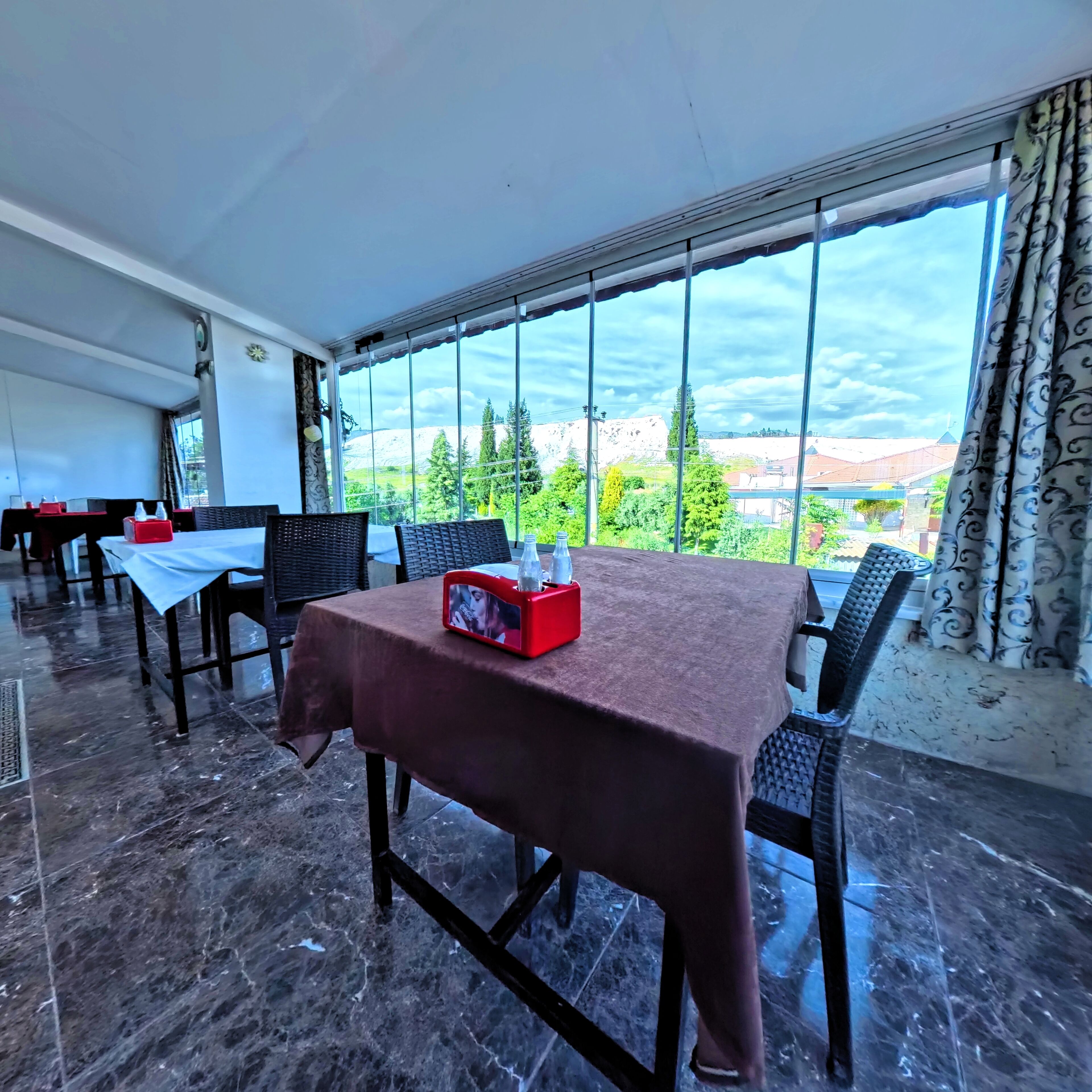 Un restaurante con una mesa lista para dos, una caja roja sobre la mesa y vistas a un paisaje montañoso a través de amplias ventanas.
