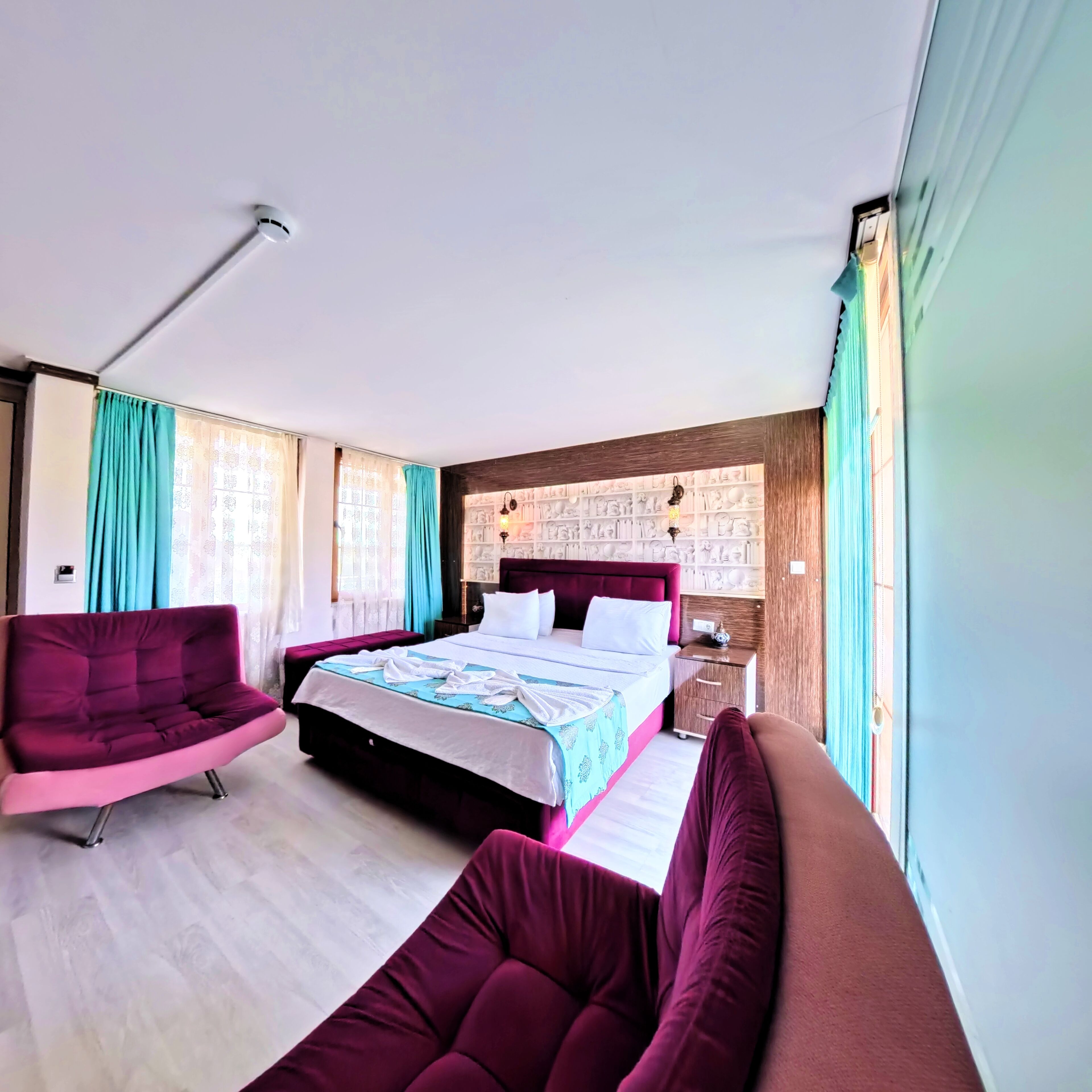 A modern hotel room with a large bed, a sofa, a desk, and a wall with decorative elements.