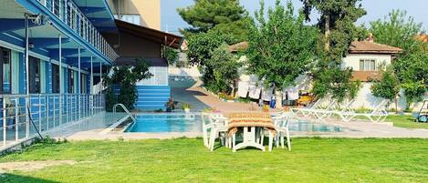 A hotel with a swimming pool, outdoor seating, and a large tree.