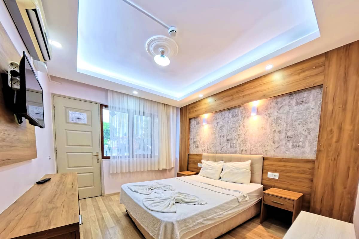 A bedroom with a bed, wooden headboard, bedside tables, a wooden desk, and a television mounted on the wall.