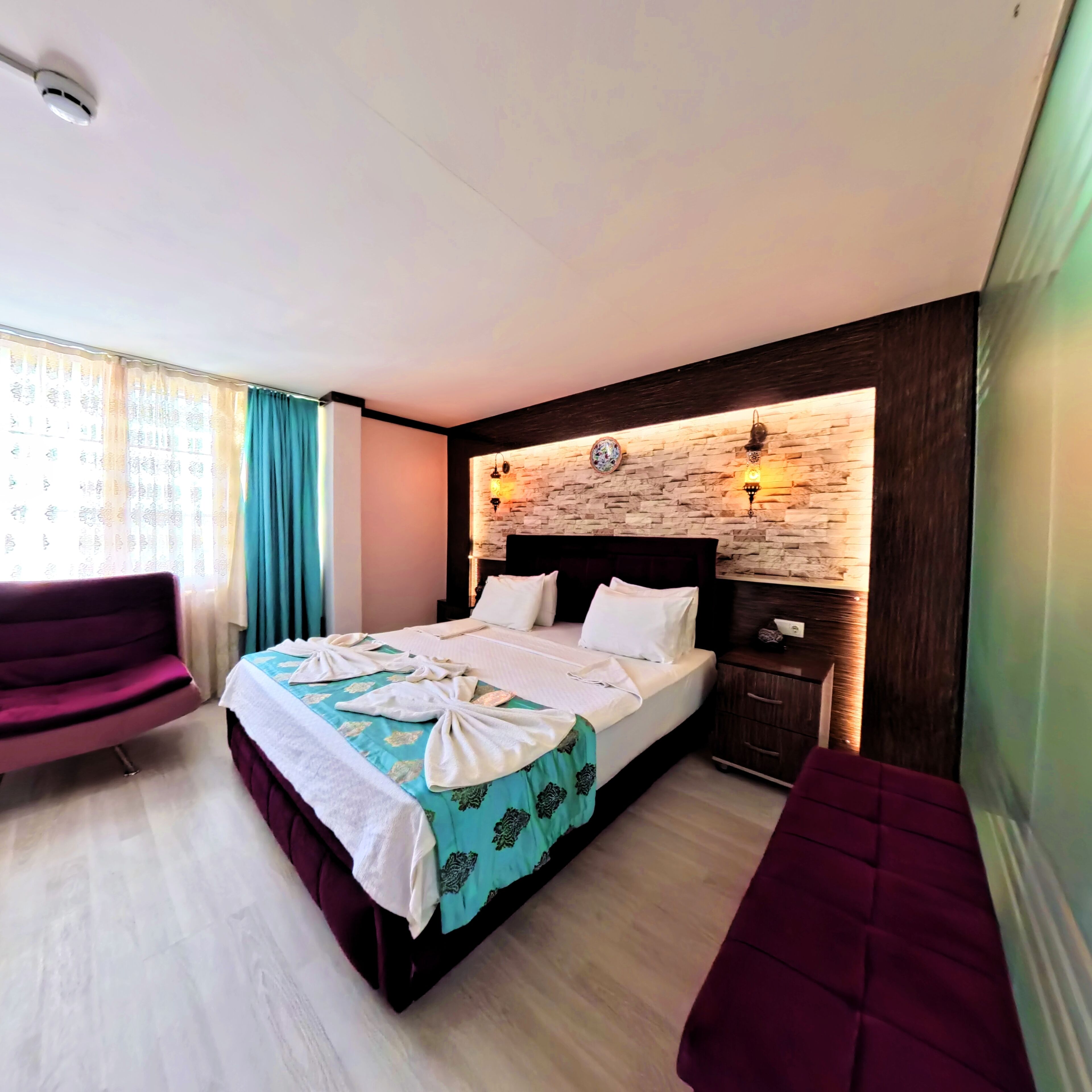 A hotel room with a bed, a nightstand, a chair, and a decorative wall.