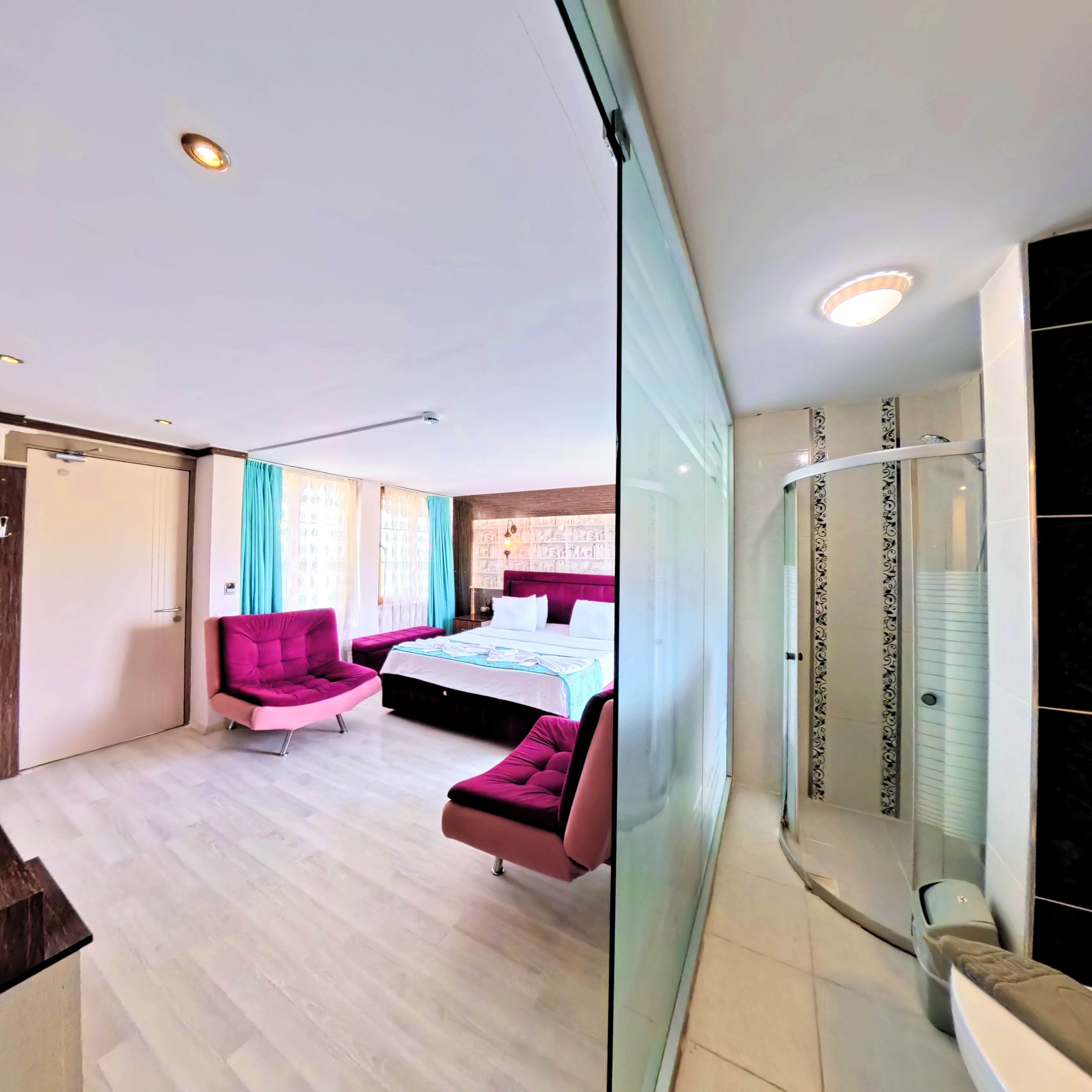 Un dormitorio moderno con una cama, dos sillas rosas, cabina de ducha de vidrio y suelo de madera.