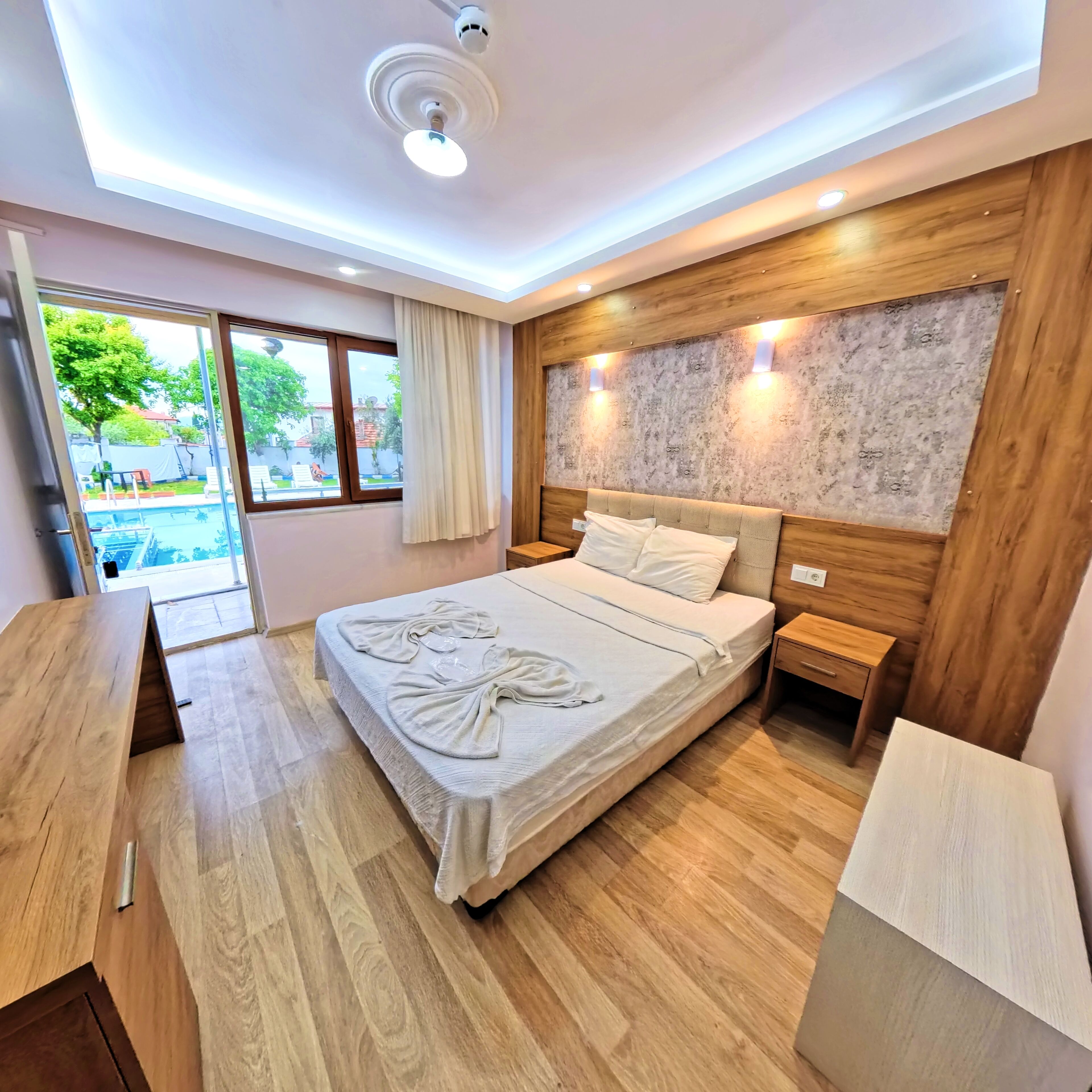 Une chambre d’hôtel avec un lit, un plancher en bois, un bureau, une table de chevet et une vue sur une piscine.