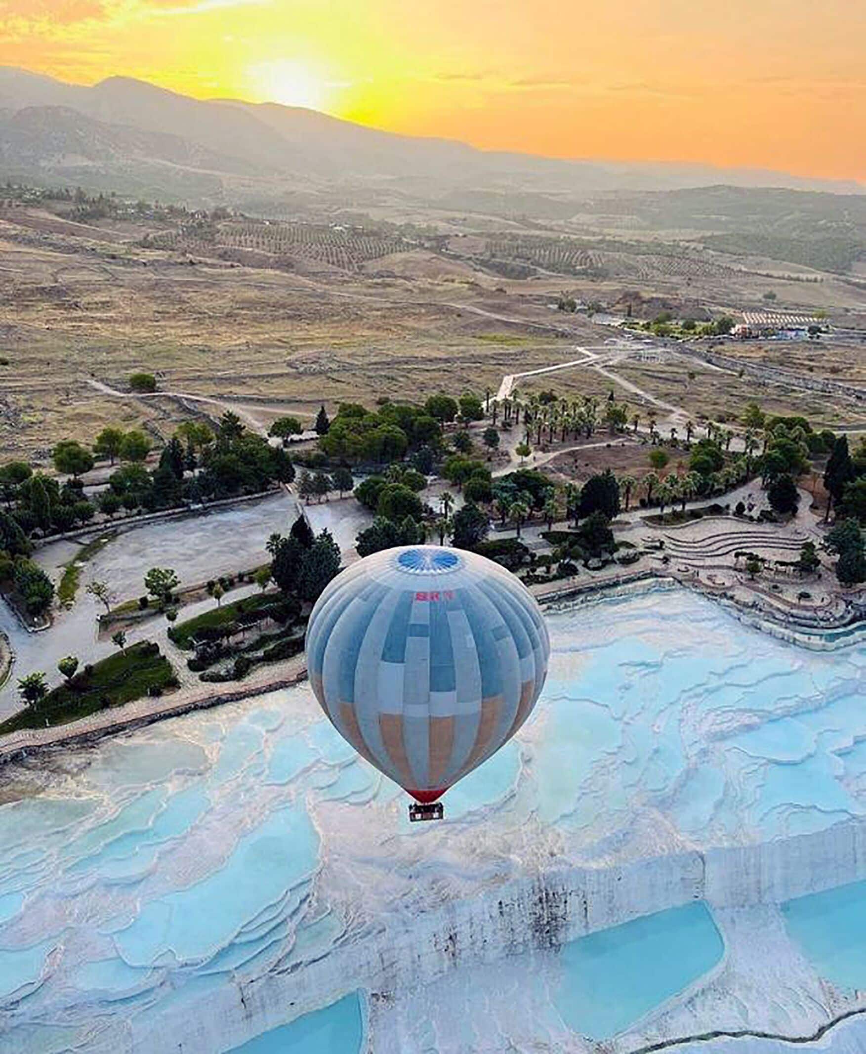 A hot air balloon over terraced pools with a landscape in the background.